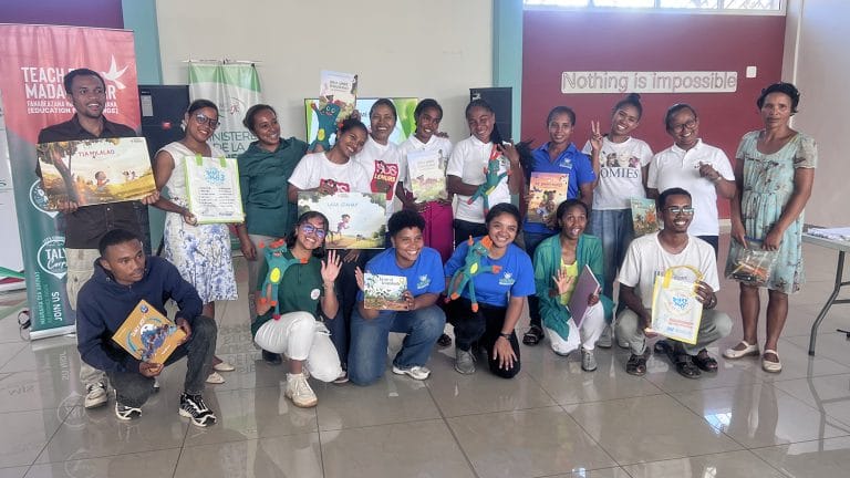 Group of young people posing with books at an indoor education event, with banners in the background.