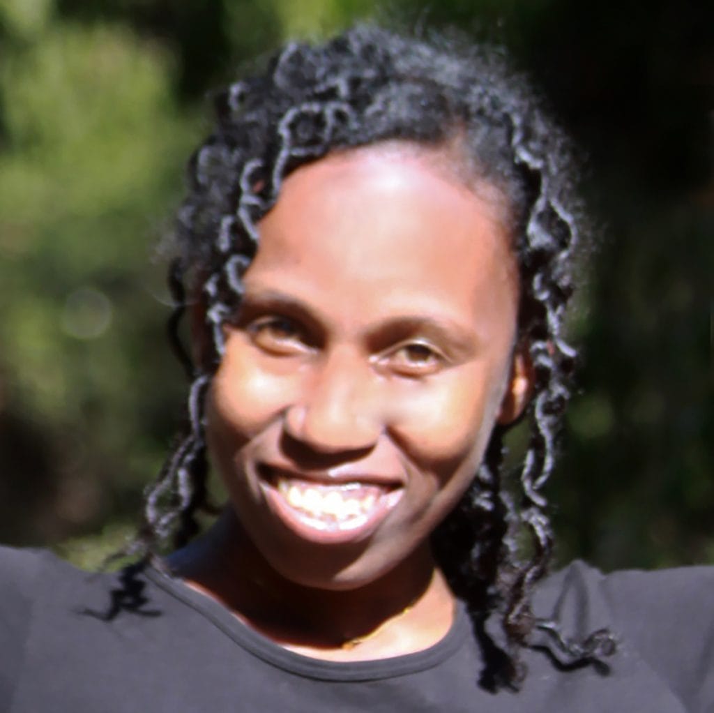 Smiling woman with long dreadlocks outdoors, wearing a dark shirt.